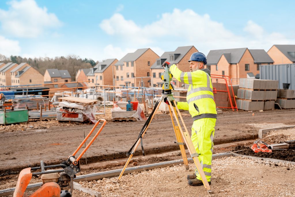 a land surveyor on a construction site, building houses, using a total station to conduct an as-built survey of the site