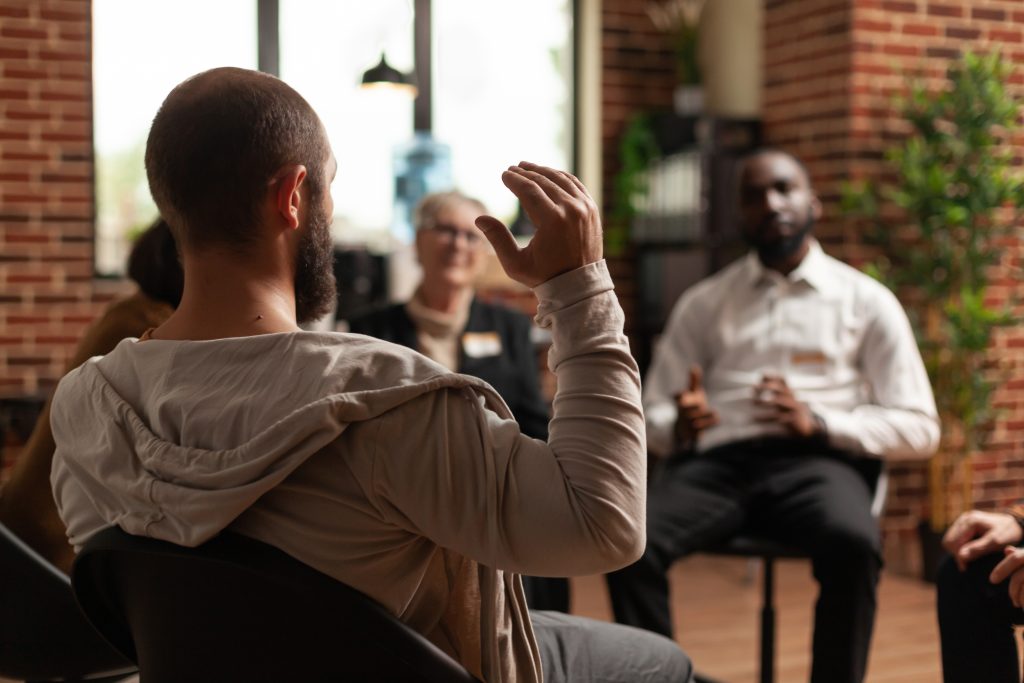 Man in a support group sharing mental health issues with group at a meeting, talking to therapist. People having conversation about depression and suicide at therapy session.