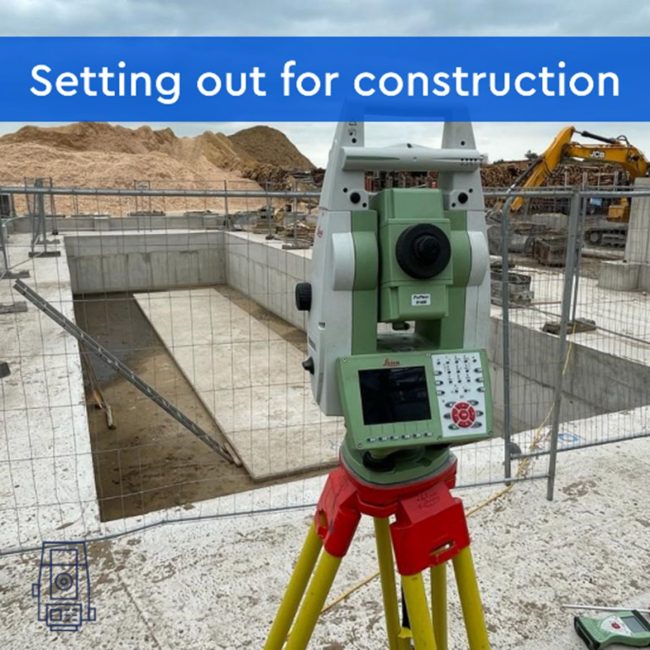 Image of a total station, facing the camera, with a construction site behind it