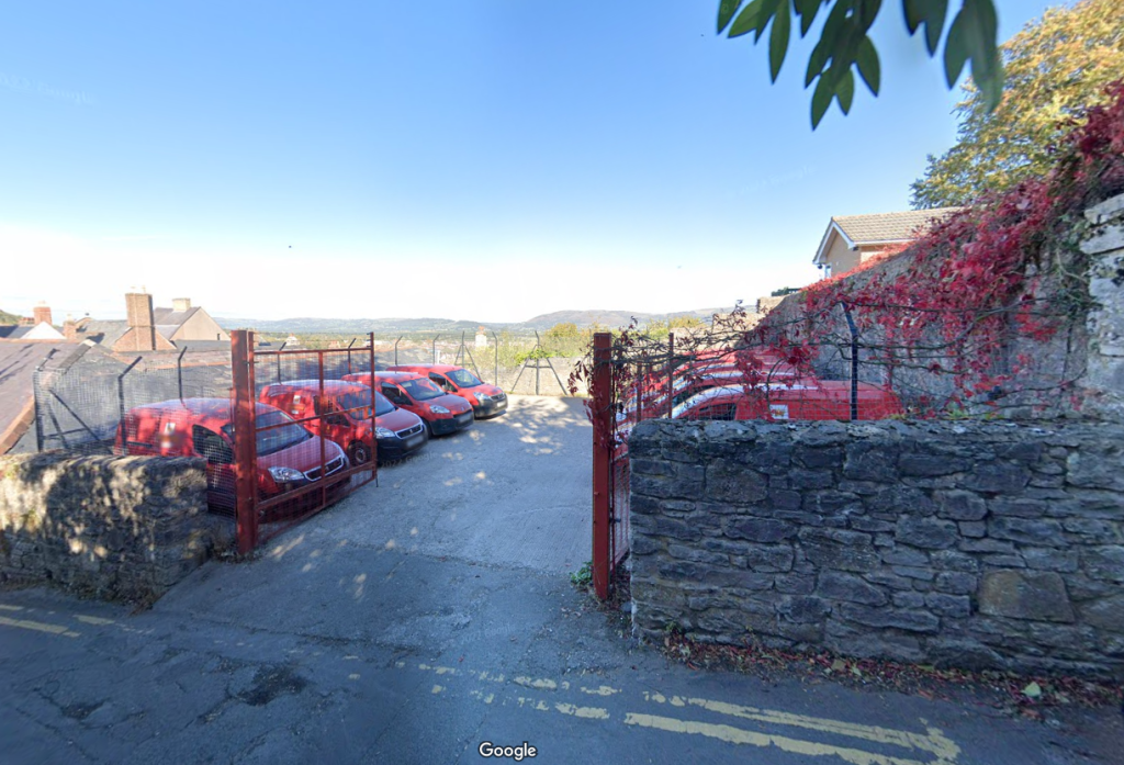 car park filled with red royal mail vans with a brick wall and foilage
